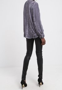 Blusa grigia a maniche lunghe, con una texture e un collo rotondo, con polsini con bottoni, abbinata a pantaloni in pelle nera attillati e tacchi alti neri.