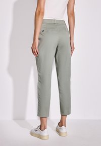 Světlé zelené zkrácené kalhoty vyrobené z hladké tkaniny. Mají plochý pas a zadní kapsy. Kombinované s bílými teniskami.