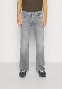 Lichtgrijze jeans met een uitlopende pasvorm, voorzien van een vervaagde textuur, vijf zakken en een knoopsluiting, gecombineerd met zwarte sportschoenen.