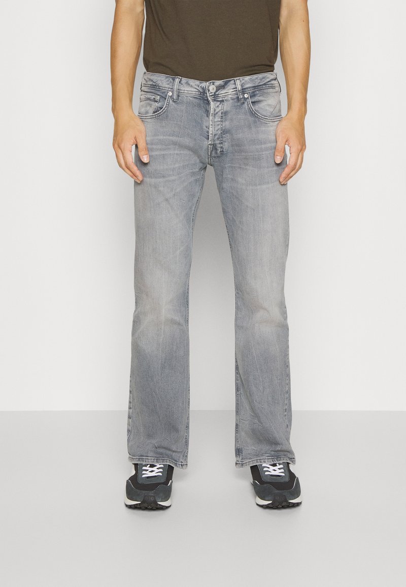 Lichtgrijze jeans met een uitlopende pasvorm, voorzien van een vervaagde textuur, vijf zakken en een knoopsluiting, gecombineerd met zwarte sportschoenen.