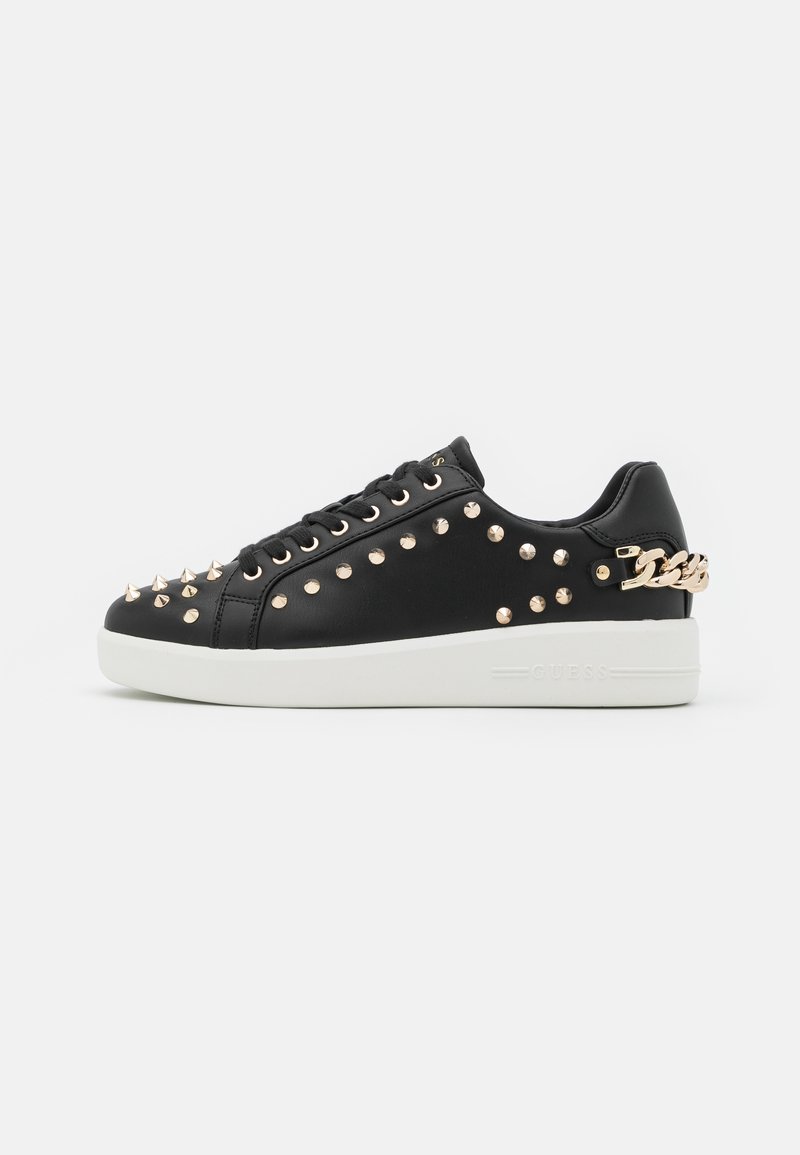 Sneaker in pelle nera con borchie in tono oro e dettagli a catena, dotato di suola bianca e chiusura frontale con lacci. Texture liscia in tutto il modello.