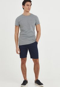 Gray short-sleeve t-shirt paired with navy shorts. Model stands with one hand in pocket, wearing black sneakers. Smooth fabric texture.