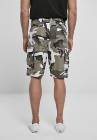 Shorts cargo camouflage aux nuances de vert, beige et blanc ; dotés de poches latérales et d'une coupe décontractée, fabriqués en tissu léger.
