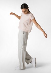 Ljust rosa, kortärmad topp med avslappnad passform; grå, vida cargobyxor med sidofickor; vita sneakers med minimalistisk design.