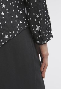 Chemise noire à manches longues avec motif d'étoiles blanches, tissu texturé. Jupe noire lisse au design simple, portée à la taille.