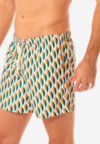 Costumi da bagno con un motivo a onde colorato in verde, arancione e bianco. Presentano un elastico in vita con cordino e tasche laterali.
