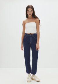 Top bianco senza spalline e jeans dritti blu scuro. I jeans hanno tasche frontali e una chiusura con bottone. Indossati con sneakers di colore chiaro.