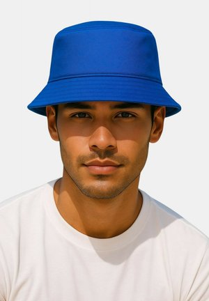 Blauwe emmerhoed van gladde stof met een brede, naar beneden gebogen rand. Draagt een effen wit T-shirt met ronde hals.