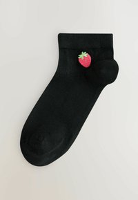 Schwarze Knöchelsocke mit einer kleinen bestickten roten Erdbeere und grünen Blättern nahe der Knöchelmanschette, auf hellem Hintergrund dargestellt.