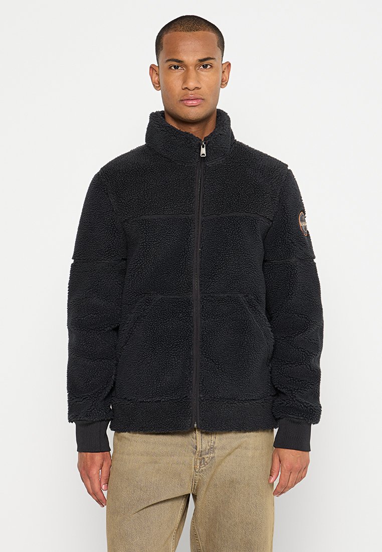 Veste en polaire noire avec un col montant, fermeture éclair à l'avant et tissu texturé. Elle comporte deux poches avant et un patch logo sur la manche.