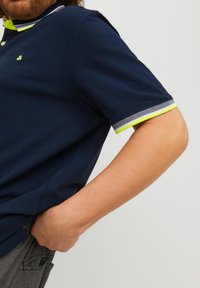 Marine blauwe polo met korte mouwen, voorzien van groene en witte gestreepte accenten op de kraag en manchetten, gemaakt van een textuur katoenmix stof.
