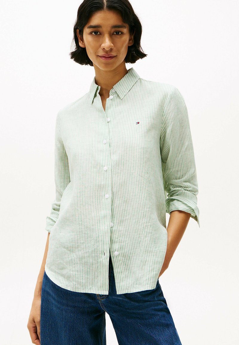 Camicia a maniche lunghe a righe verdi con bottoni bianchi e un piccolo logo sul petto; il tessuto sembra leggero e texturizzato.