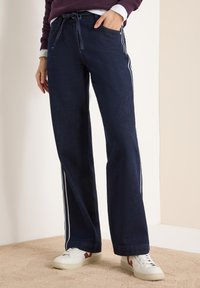 Pantalones de pierna ancha color azul oscuro hechos de denim, con rayas laterales blancas, cintura con cordón y un ajuste relajado.