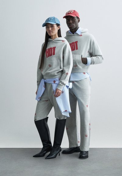 Grå hoodies och mjukisbyxor har röd text "HOT" och läpptrycksdetaljer. Blå och röda kepsar kompletterar outfitsen. Modellen bär svarta knähöga stövlar.