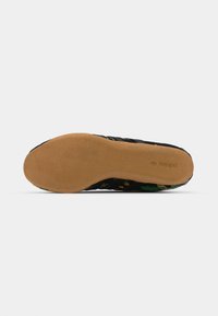 Svart slip-on sko med blommönster på ovandelen, strukturerad tyg och en slät brun gummisula för grepp.