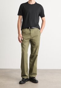 Sort bomulds T-shirt parret med olivengrønne bukser, der har en glat tekstur, lige pasform og et sort bælte med en sølvspænde.