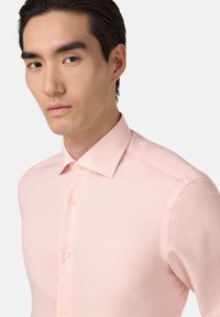 Jasnoróżowa koszula z subtelnym wzorem w paski, dopasowany krój, kołnierzyk zapinany na guziki i beżowe guziki. Gładka faktura materiału i krótkie rękawy.