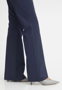 Navy blue flared pants in a smooth fabric with side seams, paired with light grey pointed-toe heels featuring a stiletto heel.