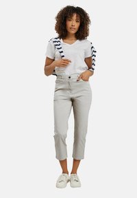 Pantalones cortos de color gris claro con una pierna ligeramente ajustada, combinados con una camiseta blanca de cuello en V y un suéter a rayas azul marino atado alrededor de los hombros.
