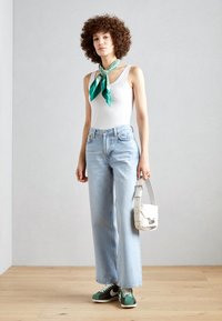 White tank top, light blue wide-leg jeans, green and white sneakers, teal and white patterned scarf, and a white crossbody bag.