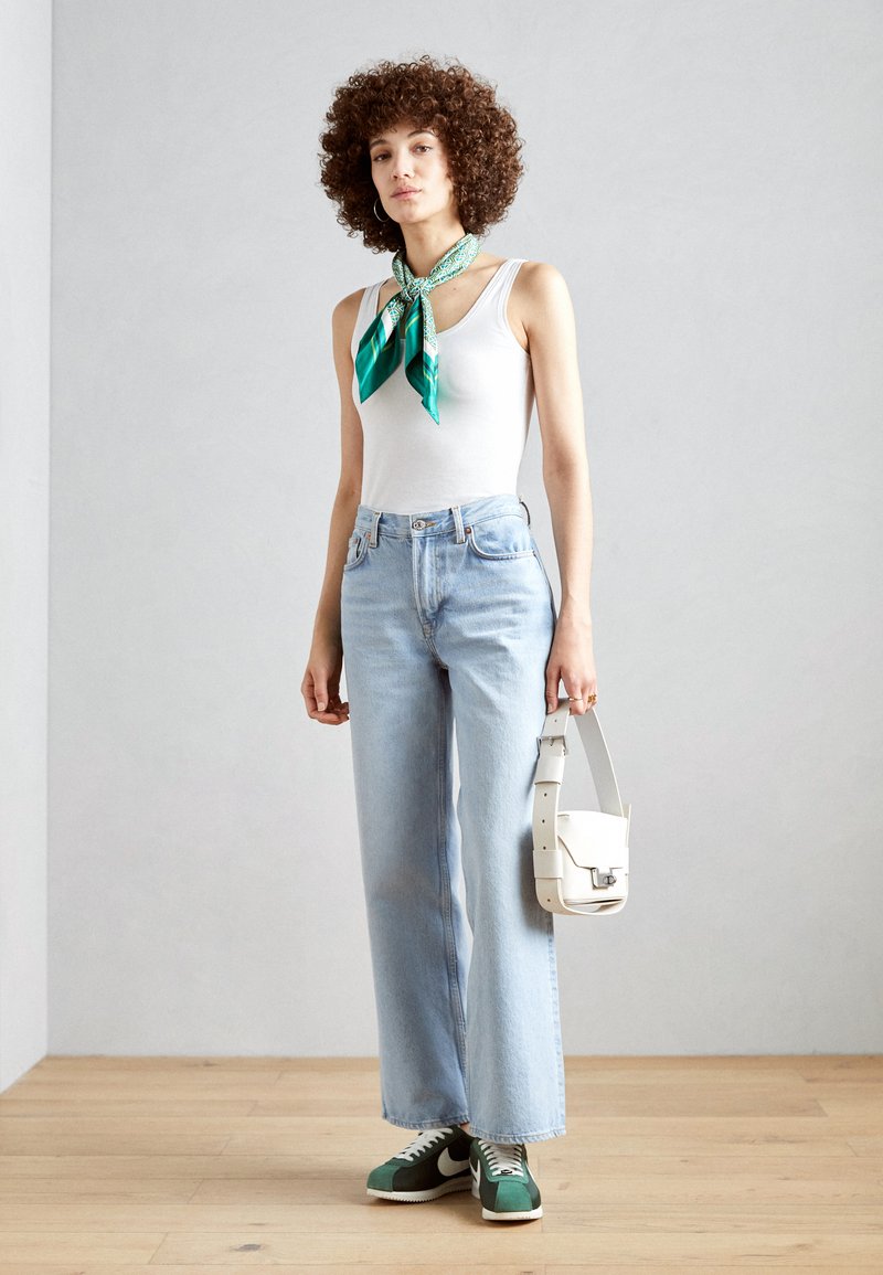 White tank top, light blue wide-leg jeans, green and white sneakers, teal and white patterned scarf, and a white crossbody bag.