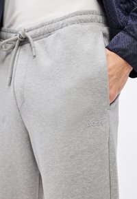 Szürke, puha anyagból készült melegítőnadrág, elasztikus derékrésszel, húzózsinórral és oldalzsebekkel. Finom "BOSS" logó részlettel.