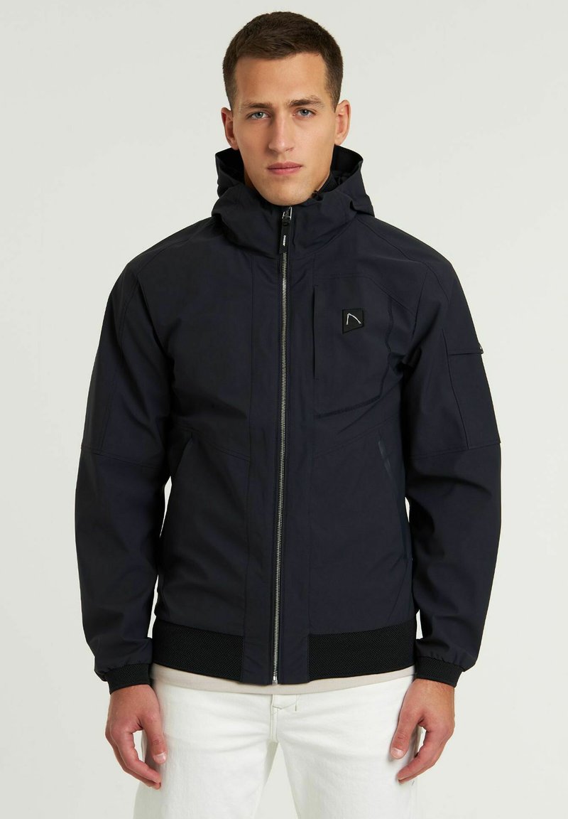 Chaqueta azul marino con capucha, cremallera frontal, puños elásticos y una cintura texturizada. Presenta un logo en el pecho y bolsillos laterales.