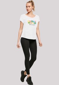 Hvit kortermet skjorte med fargerik tekstdesign; parret med svarte leggings og svarte joggesko. Glatt stoff, avslappet passform.