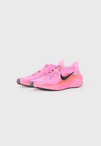 Une paire de baskets de course très brillantes de couleur rose vif avec des logos Swoosh noirs de Nike et des accents orange sur un fond blanc.