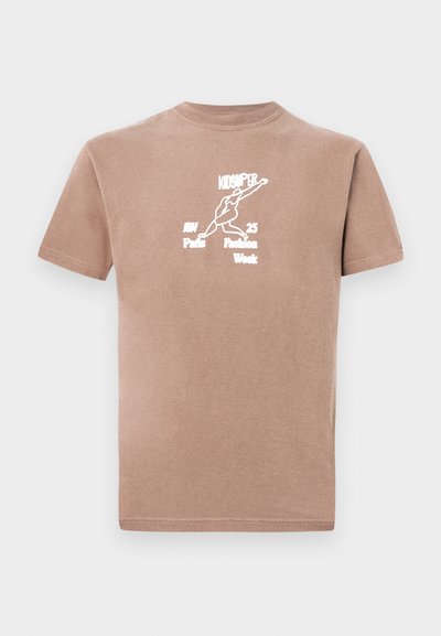 Καφέ βαμβακερό T-shirt με κοντά μανίκια, με λευκό γραφικό εκτύπωση που απεικονίζει μια φιγούρα και κείμενο: "KIDSUPER AW Paris Fashion Week."