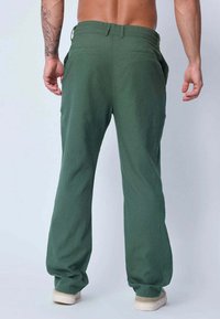 Pantalons verts, amples, en tissu léger, dotés de deux poches arrière et d'une coupe droite avec une texture naturelle.