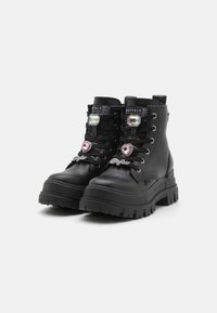 Botas de tobillo de cuero negro con suela gruesa, con acentos decorativos de corazones y gemas en la parte delantera y etiquetas de marca en el cuello.