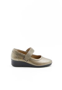 Zapato cerrado, de cuña baja en dorado metálico con una correa ajustable texturizada y suela negra contrastante. Parte superior de cuero suave.
