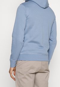 Sudadera de color azul claro hecha de una tela suave, con un bolsillo canguro, puños y dobladillo acanalados, y capucha con cordón para ajustes.