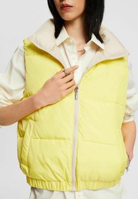 Gilet imbottito giallo chiaro con collo alto color crema, chiusura con zip frontale, orlo elastico e tasche laterali; dettaglio a trama trapuntata.