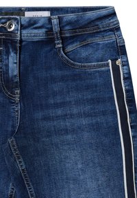 Jeans de mezclilla azul oscuro con una textura suave, que cuentan con una franja lateral de contraste y bolsillos estándar. Cierre de botón y cremallera.