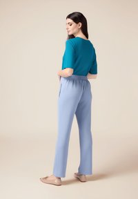 Haut à manches courtes bleu canard associé à un pantalon léger à taille élastique bleu clair. Texture lisse, coupe droite, et ballerines de couleur neutre complètent le look.