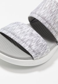 Sandal grigio con due larghe cinghie in tessuto che presentano un motivo testurizzato e una spessa suola bianca su uno sfondo bianco.