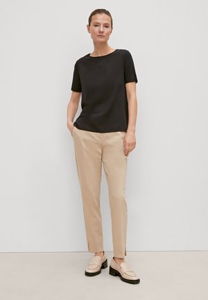 Black short-sleeve T-shirt paired with beige slim-fit trousers and light-colored loafers. Smooth fabric with subtle details.