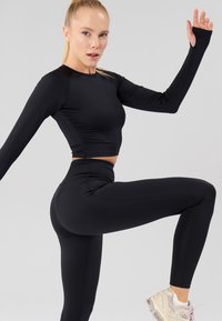 Zwarte sporttop met lange mouwen en hoge taille legging, slim fit ontwerp met een gladde textuur. Opvallende stikseldetails; model in actieve pose.