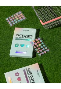 Emballage Cute Dots en vert clair avec des accents holographiques ; comprend des patchs en forme d'étoile, de cœur et de fleur. Le fond est en gazon artificiel.