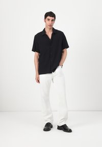 Camicia a maniche corte a strisce nere con chiusura a bottoni, abbinata a pantaloni bianchi e scarpe nere, caratterizzata da una vestibilità rilassata e una texture liscia.