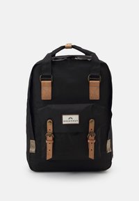 Sac à dos en tissu noir avec des sangles en cuir marron, une poche avant et une étiquette de marque. Il dispose de quincaillerie métallique et d'accents texturés.