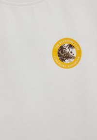 Tissu blanc avec un petit logo circulaire jaune montrant des palmiers et le texte de plage « The Seashore Club Echo Point, Bayangan. »