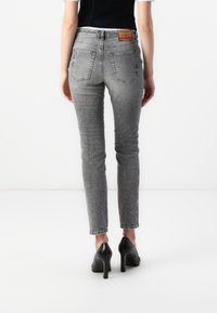 Fitted gray jeans with a subtle wash, five pockets, and a branded back patch, paired with black high-heeled shoes.