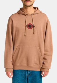 Sudadera marrón con un bolsillo frontal, cordones, y un gráfico circular con acentos rojos y negros. Presenta un ajuste relajado y un material suave.
