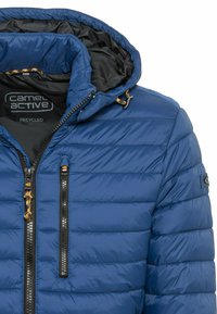 Blå pufferjakke lavet af genbrugsmateriale, med horisontalt quiltet design, en lynlås lukning og en hætte med snorede detaljer.