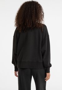 Felpa nera oversize con spalle scese, polsini e orlo a coste. Il materiale sembra morbido e di consistenza. Design semplice, senza motivi visibili.