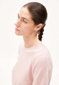 Light pink knitted sweater with a round neckline, smooth texture, and long sleeves. Model has a braid and minimal jewelry.