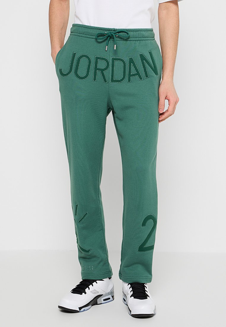 Pantalons de jogging verts en tissu doux, avec un grand texte "JORDAN" à l'avant et des accents numériques sur les jambes. Taille ajustable.